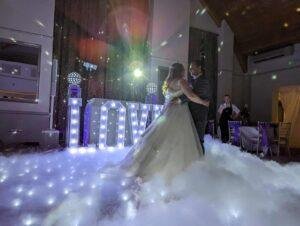 Wedding couple dancing with illuminated "LOVE" sign at reception.