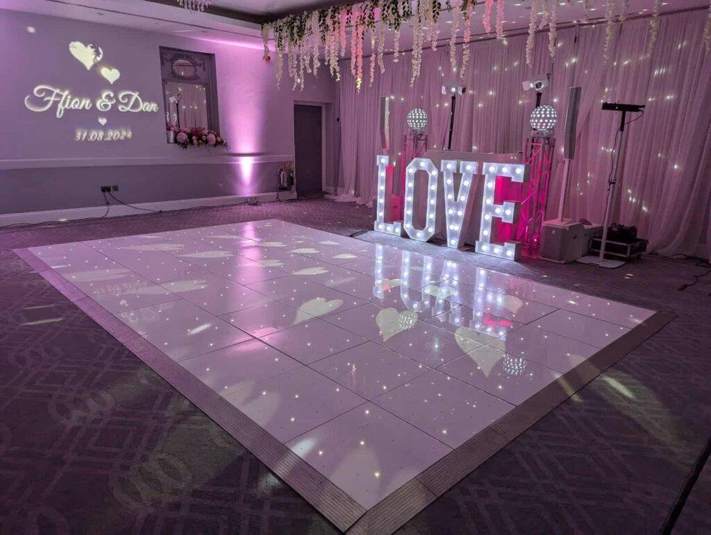 Elegant wedding dance floor with illuminated "LOVE" sign, fairy lights, and romantic pink lighting f.