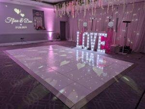 Elegant wedding dance floor with illuminated "LOVE" sign, fairy lights, and romantic pink lighting f.
